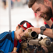 Uniformed officer showcases artillery to young boy.