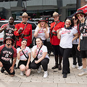 Male and female cheer squad dressed in black, red and white post with two officers in red serge.