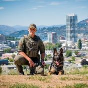 An RCMP officer in a tactical uniform is next to a German Shepherd dog.