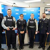 Six policiers de la GRC faisant face à la caméra devant une toile de fond de la région du Centre de la GRC.