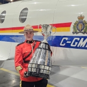 An officer in Red Serge poses with the Grey Cup in front of an RCMP plane.