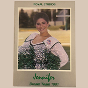 A female cheerleader with green and white pom-poms poses and smiles for the camera.