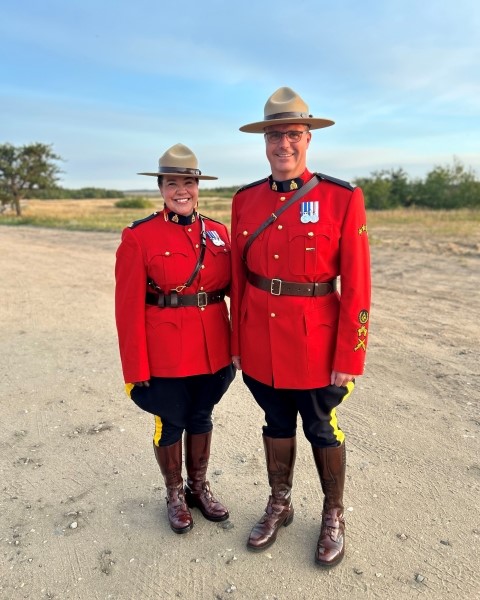 A male and female officer dressed in Red Serge pose on a dirt road with a field in the distance.