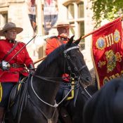 Two Mounties horseback. The woman carries a sword, and the man carries a flagpole with the RCMP's regimental crests on display.