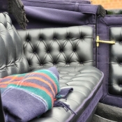 A blue, green and red blanket lies folded on the black leather seat inside an open horse carriage.